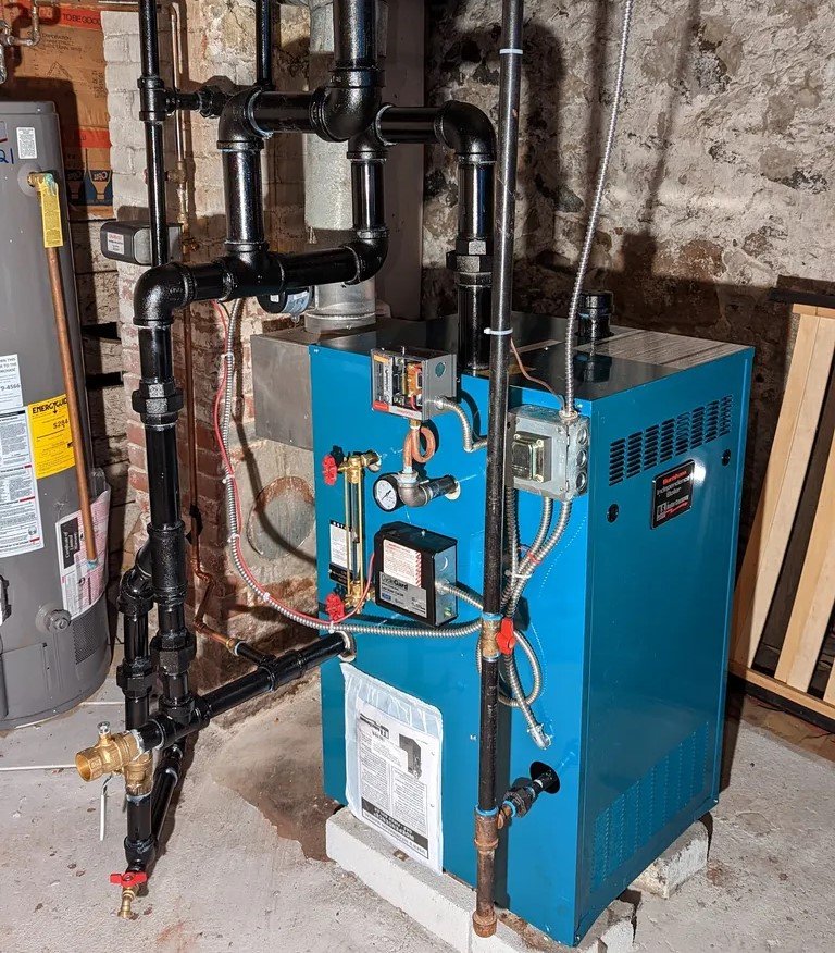 A high-efficiency blue boiler system installed in a residential basement, complete with black pipes and a connected gauge system, providing reliable heating services in Greater Boston, MA.
