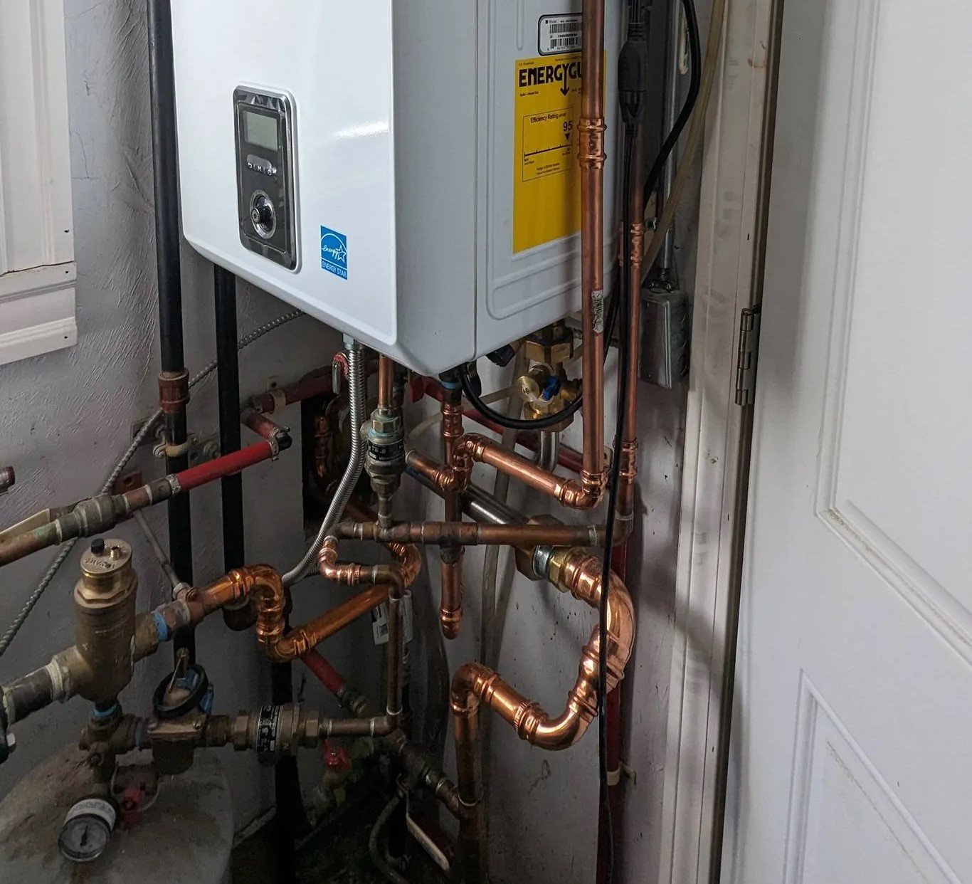 A Navien tankless water heater installed in a home, surrounded by a network of copper pipes and fittings for efficient water heating and HVAC services in Boston, MA.