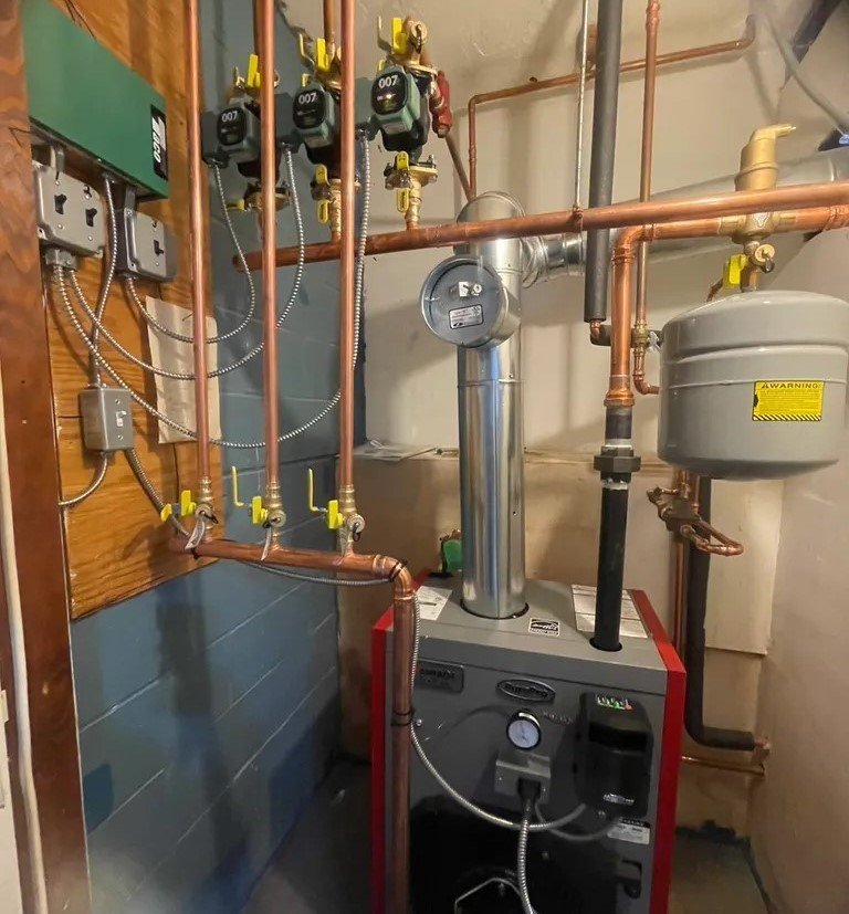 An indoor boiler system with multiple copper pipes, pumps, and gauges installed for residential heating.